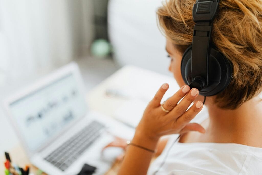 Woman wearing large headphones, working on a laptop in a home office setup, focused on her screen.